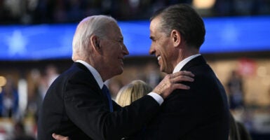 President Joe Biden and his son Hunter Biden, both dressed in black suits, smile at each after sharing a hug.