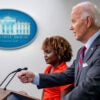 President Joe Biden, wearing a gray suit and a red-striped tie, speaks during a White House press briefing as he stands beside White House press secretary Karine Jean-Pierre, who is wearing a bright orange blouse.