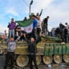 Syrians celebrate while standing on top of a military tank.