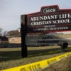 Yellow crime scene tape drapes around a black school sign with white lettering for Abundant Life Christian School.