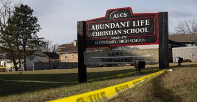 Yellow crime scene tape drapes around a black school sign with white lettering for Abundant Life Christian School.