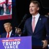 Virginia Gov. Glenn Youngkin talks at a podium with Donald Trump in the background.