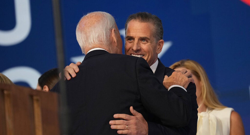 Hunter Biden in a black suit hugs his father, Joe Biden, also in a black suit.