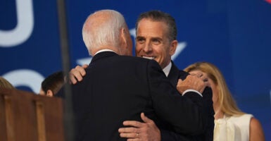 Hunter Biden in a black suit hugs his father, Joe Biden, also in a black suit.