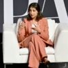 Lina Khan sits in a sofa couch seat with her legs crossed while speaking.