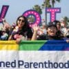 A group of people hold up a Planned Parenthood rainbow sign with the letters spelling out "Vote" behind them.