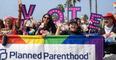 A group of people hold up a Planned Parenthood rainbow sign with the letters spelling out "Vote" behind them.