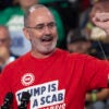 UAW chief Shawn Fain raises his fist while wearing a shirt reading "Trump Is a Scab."