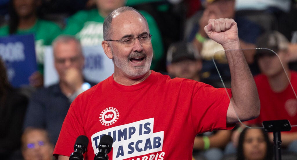 UAW chief Shawn Fain raises his fist while wearing a shirt reading "Trump Is a Scab."