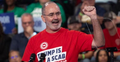 UAW chief Shawn Fain raises his fist while wearing a shirt reading "Trump Is a Scab."