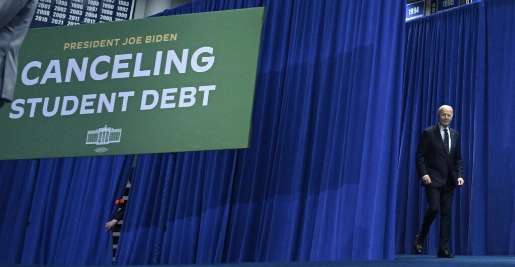 President Joe Biden walks off stage with a large canceling student debt banner hanging behind him.