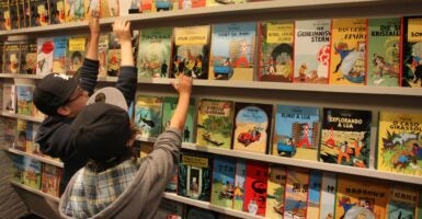 Children reach for the Tintin books on a shelf.