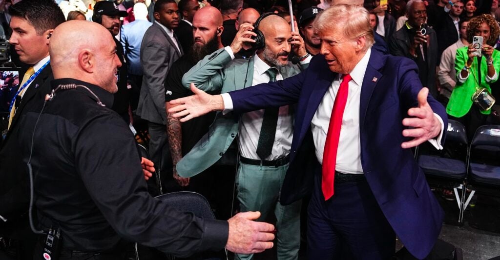 Donald Trump and podcaster Joe Rogan prepare to embrace each other.