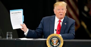 Donald Trump stands at a podium holding up a report while promoting his plan to cut taxes.