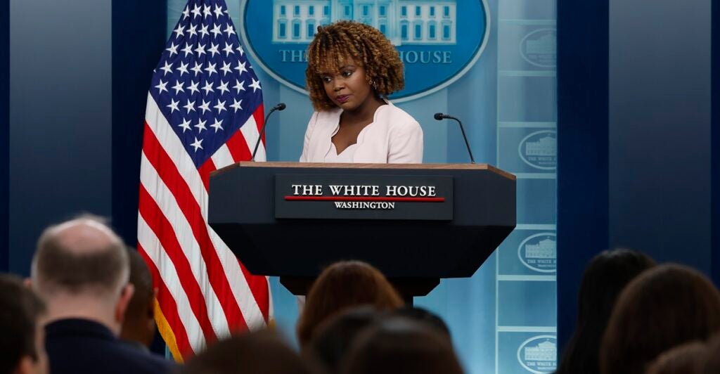 White House press secretary Karine Jean-Pierre speaks during a news conference, standing next to an American flag.