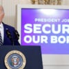 Joe Biden in a blue suit at a podium in the White House with a large TV screen behind him that reads President Joe Biden: securing our border