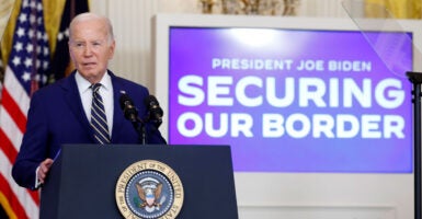 Joe Biden in a blue suit at a podium in the White House with a large TV screen behind him that reads President Joe Biden: securing our border