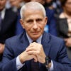 Dr. Anthony Fauci sits behind a desk, hands clasped, wearing a frown.