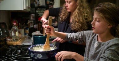 Mother and young daughter cook side-by-side at a gas stove