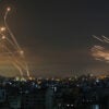 Israel's missile defense system intercepts rockets over Israel, bright orange rockets in the dark sky above city buildings.