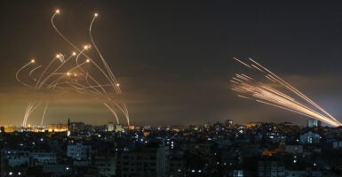 Israel's missile defense system intercepts rockets over Israel, bright orange rockets in the dark sky above city buildings.