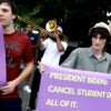 three college-age men hold up signs asking President Biden to cancel student debt