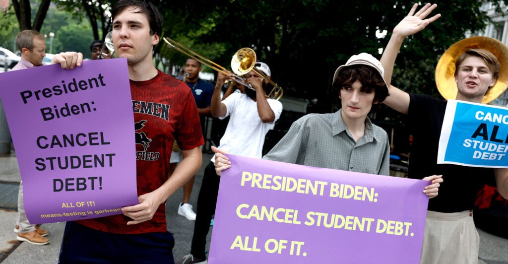 three college-age men hold up signs asking President Biden to cancel student debt