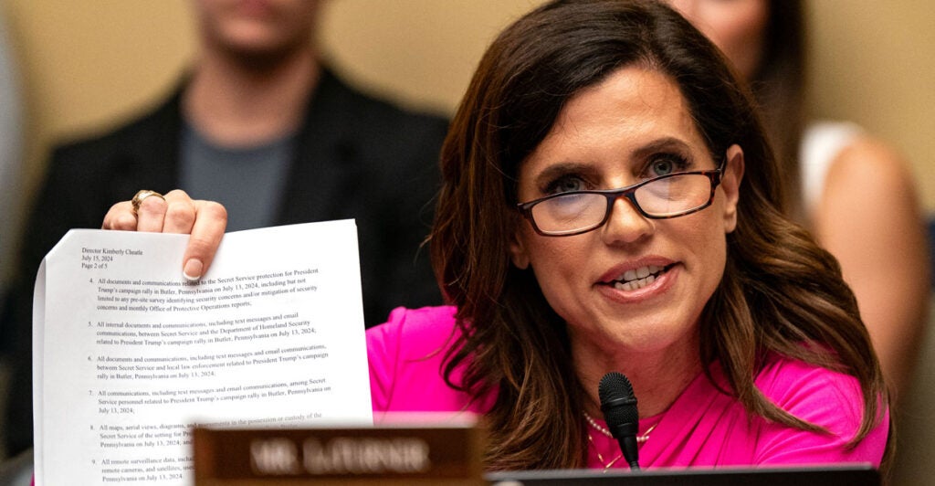 Congresswoman Nancy Mace in a pink top and glasses holding up a piece of paper and talking to a witness at a House hearing