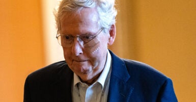 Mitch McConnell, in a blue suit, walks down an orange Senate hallway, with a frown on his face.