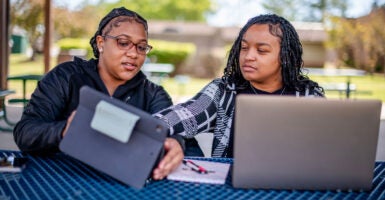 Two black female students studying together, looking at their laptops and tablets