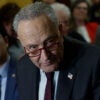 Senate Majority Leader Chuck Schumer, in a black suit and glasses, stares ominously during a conference.