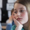 Elementary school girl with long hair staring off in class, bored.