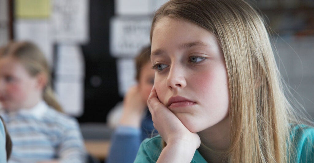 Elementary school girl with long hair staring off in class, bored.