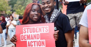 Two students smile and hold a sign that reads, "Students Demand Action."