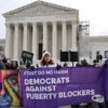 Protestors stand outside of the Supreme Court, holding a banner that reads, "Democrats against puberty blockers."