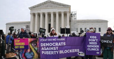 Protesters stand outside of the Supreme Court, holding a banner that reads, "Democrats against puberty blockers."