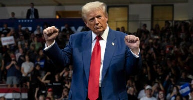 Donald Trump, in a navy suit and red tie, dances with his fists in the air on stage.