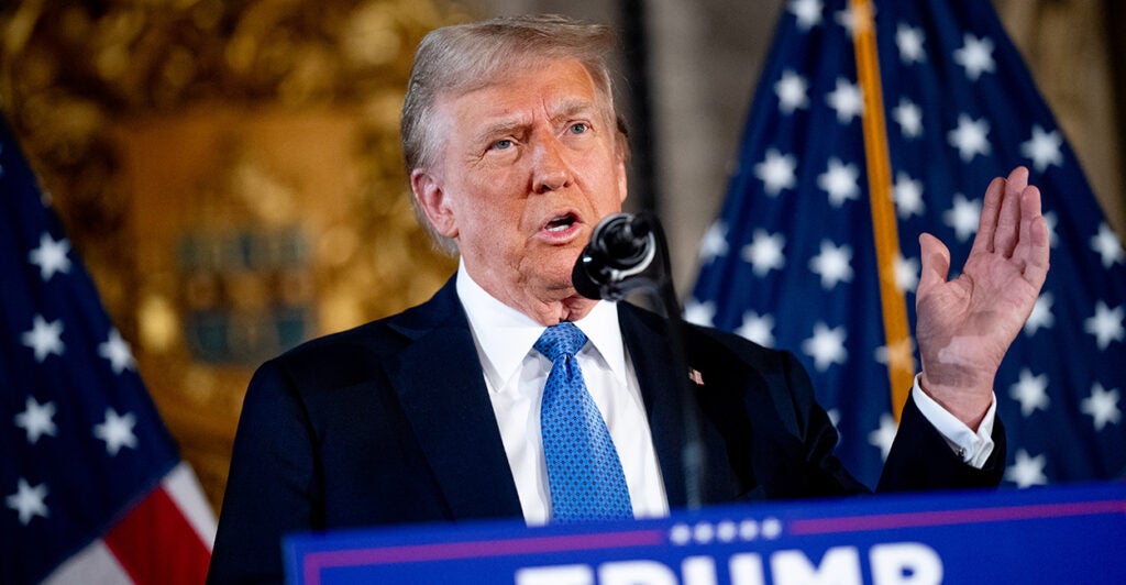 Trump, in a navy suit and a bright blue tie, stands behind a podium and speaks at a news conference at his Mar-a-Lago.