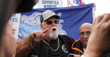 Longshoremen's union leader Harold Daggett in a black T-shirt and jacket with sunglasses and a baseball cap gestures by pointing his finger while talking to striking dockworkers