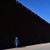 A cattle rancher walks a road running along the U.S.-Mexico border and a 30-foot tall section of the border wall.