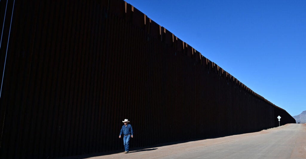 A cattle rancher walks a road running along the U.S.-Mexico border and a 30-foot tall section of the border wall.