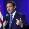 Florida Gov. Ron DeSantis speaking into a hand-held microphone with a U.S. flag as backdrop