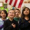 Elementary school-age children pledge allegiance to the American flag.