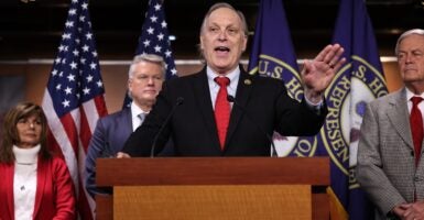 Andy Biggs holds his left hand up in the air while talking while standing at a podium.