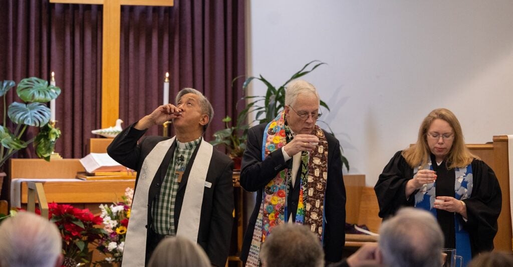 Two reverends stand in front of the congregation and participate in the Holy Communion.