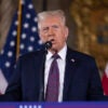 Donald Trump gestures in a suit in front of two American flags