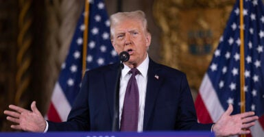 Donald Trump gestures in a suit in front of two American flags