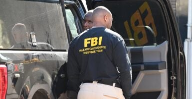 A man wearing an FBI jacket stands near a vehicle.