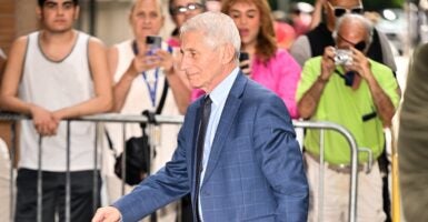 Anthony Fauci walks outdoors into the entrance of a building.