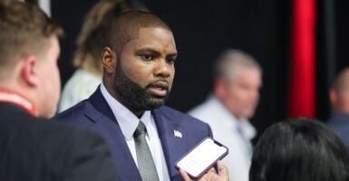 Byron Donalds, wearing a blue suit and grey necktie, answers questions into a mobile phone.